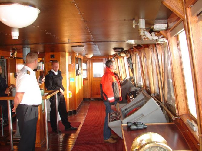 A master, seaman, and harbor pilot in a ship’s wheelhouse